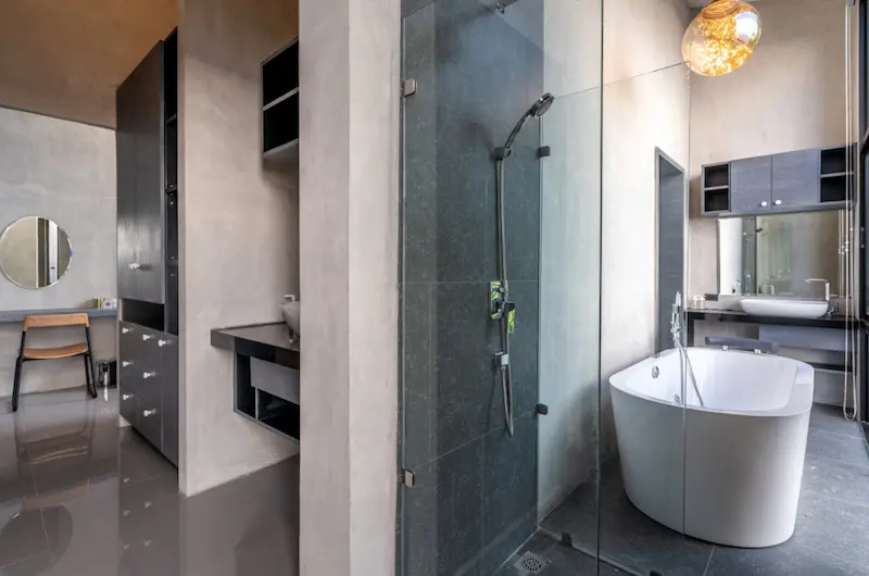 Baño amplio con paredes de acabado cemento, ducha con mampara de cristal y bañera exenta junto a un lavabo suspendido