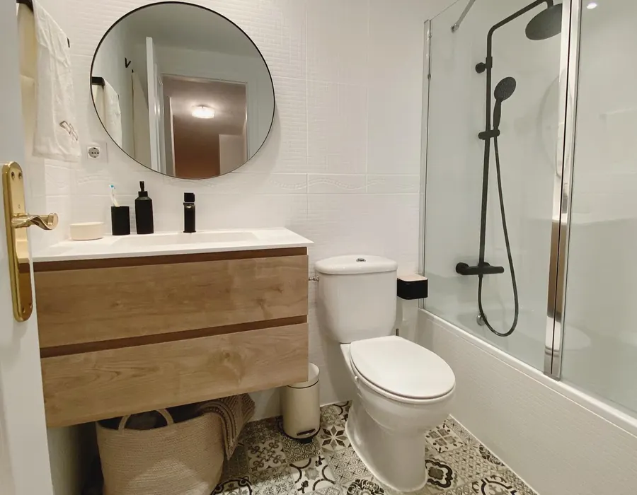 Baño reformado con suelo hidráulico, mueble de madera y ducha con grifería negra