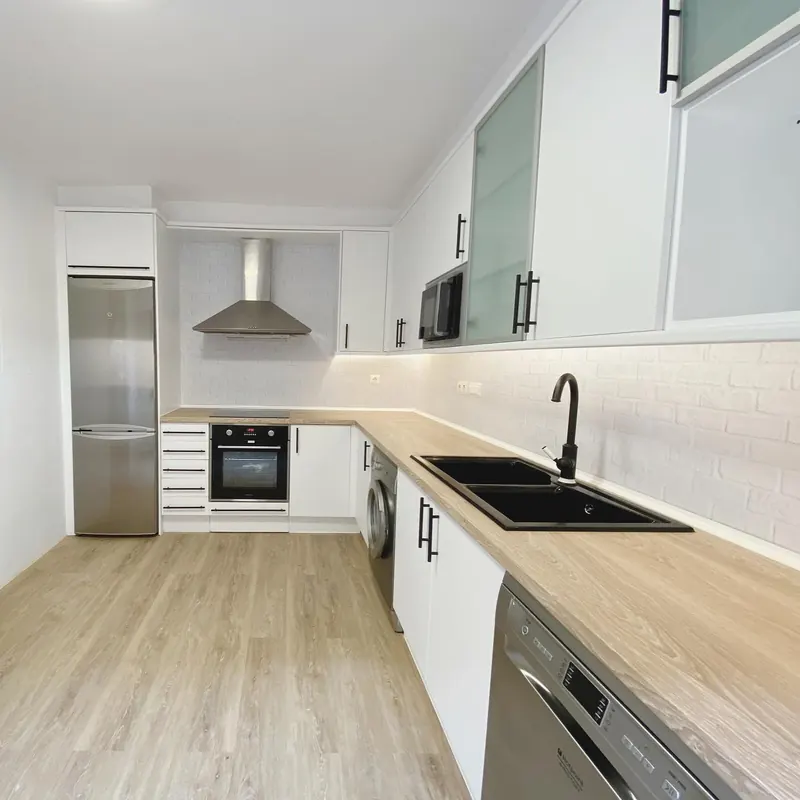 Cocina reformada con muebles blancos y encimera de madera