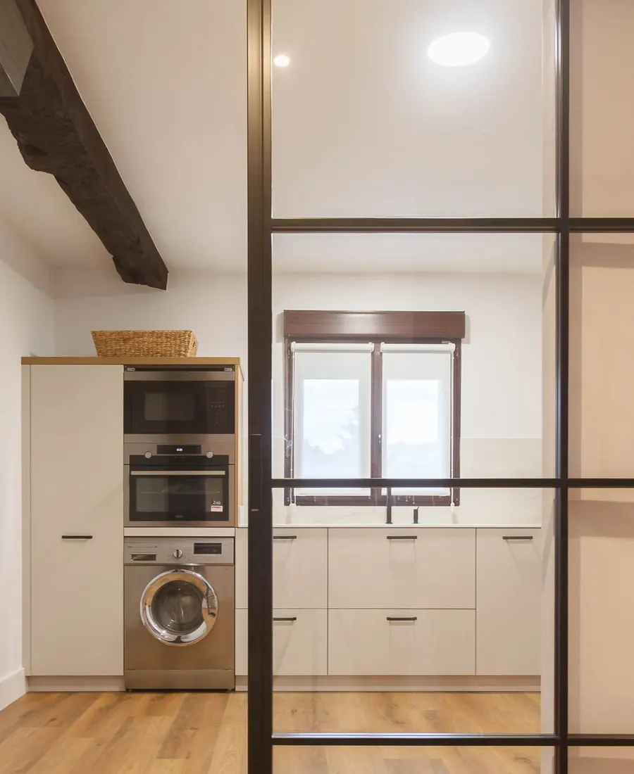 Cocina reformada con viga de madera vista y cerramiento de cristal con perfilería negra