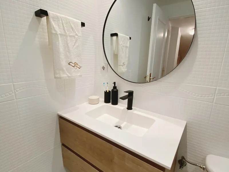 Baño reformado con mueble de madera, lavabo integrado y espejo redondo