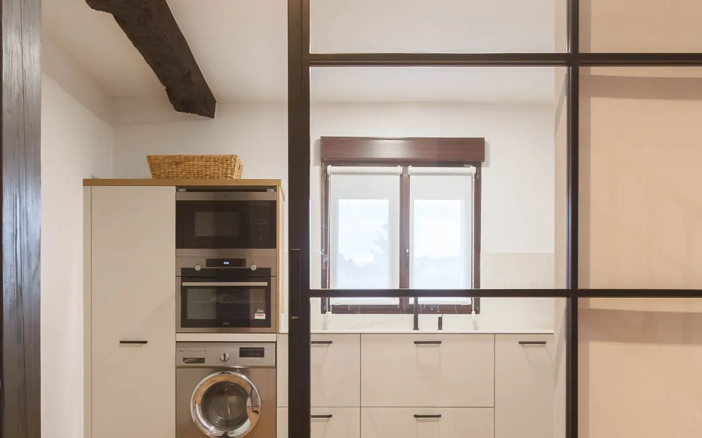 Cocina reformada con viga de madera vista, muebles claros y cerramiento de cristal